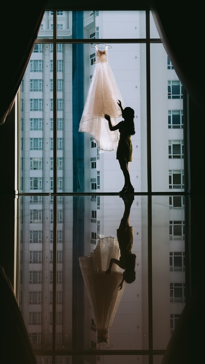 女人的白色礼服挂在透明玻璃窗口
